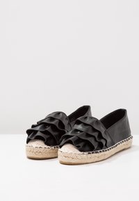 Espadrillas nere con una parte superiore sintetica arricciata, punta rotonda e suola in fibra naturale intrecciata con un resistente bordo in juta.