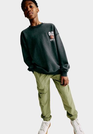Felpa grigia con grafica di una palma; pantaloni cargo in verde oliva; sneakers bianche; vestibilità rilassata; polsini e vita a costina.
