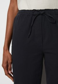Dark blue elastic-waist pants with a drawstring closure and side pocket. Made from soft material, featuring a smooth texture and casual fit.
