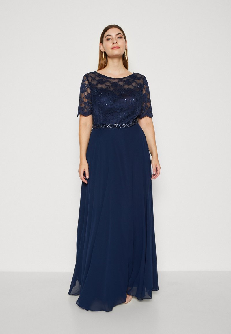 Rochie de seară bleumarin cu mâneci scurte din dantelă și un brâu decorat cu mărgele. Fusta fluidă este realizată dintr-un material moale și ușor.