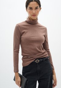 Barna bordázott garbó, hosszú ujjakkal, amelyet magas derekú fekete farmernadrággal és fekete clutch táskával párosítottak. Arany övcsattal rendelkezik.