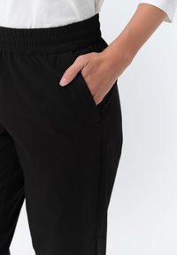 Zwarte lichtgewicht broek met een elastische tailleband en zijzak, met een gladde textuur en een getailleerde pasvorm.