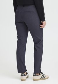 Navy slim-fit trousers with a smooth texture, featuring back pockets, paired with beige and black low-top sneakers.