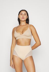 Bralette beige con spalline sottili e design a scollo a V; slip alta vita beige con pannelli in rete sui lati. Texture liscia, dettagli minimi.