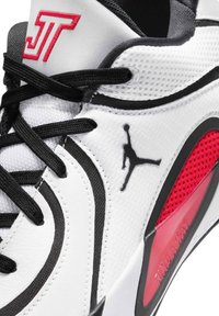 Witte en zwarte basketbalschoen met rode accenten, zwart Jumpman-logo, zwarte veters en "J T" in rood geborduurd op de tong.