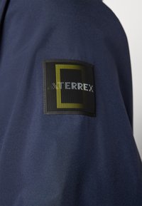 Navy blue fabric features a textured, rectangular black patch with vertical lines and the word "TERREX" in white lettering.