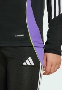 Svart sporttop med lila och gröna sidodetaljer, med en logo som säger "AEROREADY", matchad med svarta byxor och en vit logodetalj.