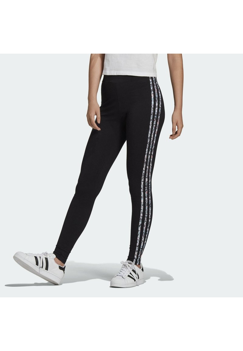 Svarta leggings med en tight passform, med blommönstrade sidostrekar. Slät tyg och ankellång klippning, i kombination med vita sneakers.
