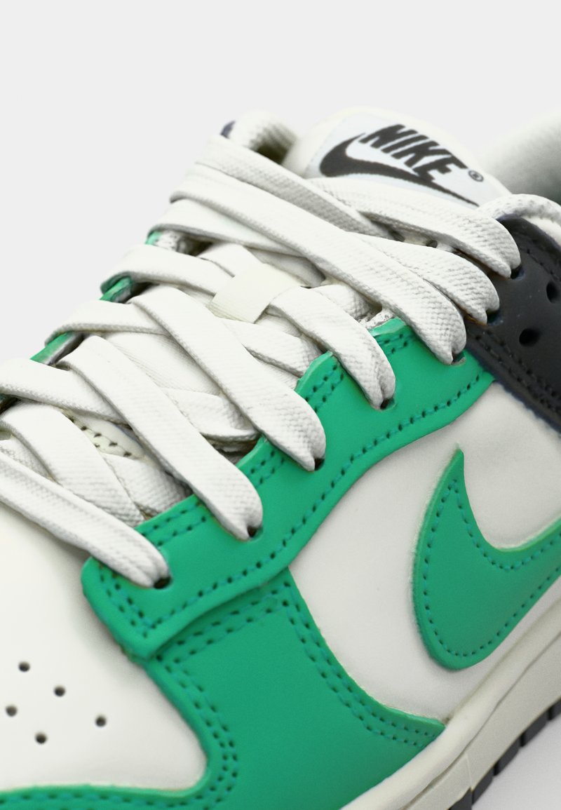 Sneaker Nike en cuir blanc avec des accents verts et gris, des superpositions texturées, des lacets blancs et des détails perforés.