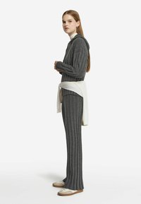 Grå ribbet hoodie med lynlås foran, parret med matchende ribbet bukser. En hvid sweater er bundet om livet. Lyse sneakers med accenter.