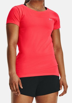 Femme portant un t-shirt de sport rouge vif à manches courtes et un short noir, montrée des épaules jusqu'au milieu des cuisses sur fond blanc.
