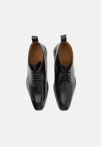 Bottines en cuir noir avec un bout pointu, une finition texturée, un design à lacets et des tirettes à l'arrière pour un enfilage facile.