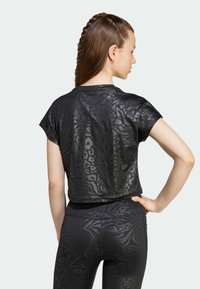 Camiseta negra corta con un estampado de animal texturizado, mangas cortas y un corte relajado, combinada con leggings negros a juego con el mismo patrón.