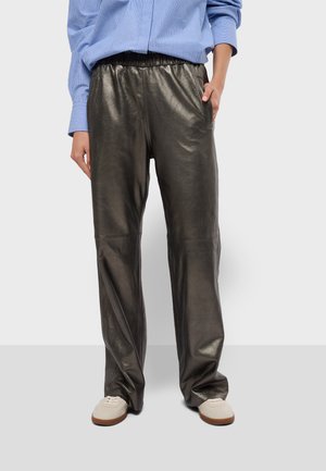Pantalon gris métallisé avec une taille élastique, coupe ample et texture lisse. Associé à une chemise rayée bleue et des baskets claires.