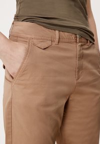 Ljusbruna bomullsbukser med en mjuk textur, som har framfickor och en subtil diamantformad detalj på bakfickan.