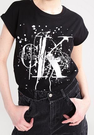 T-shirt in cotone nero con maniche corte, caratterizzato da una stampa a macchie bianche e il testo 'Calvin Klein Jeans' al centro.