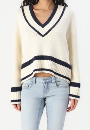 Maglione lavorato a maglia color crema con scollo a V blu navy, polsini e orlo a coste. Design cropped con strisce blu navy alla base e alle maniche.