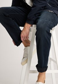 Witte sneakers met een gestructureerde zool, gecombineerd met donkere denim jeans die bij de boorden zijn opgerold, met een gladde afwerking en een aansluitende pasvorm.