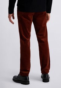 Brown corduroy trousers with a textured surface, slim fit design, and black lace-up shoes featuring decorative perforations.