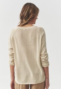 Beżowy sweter z dzianiny z okrągłym dekoltem, podwiniętymi rękawami i teksturowanym materiałem. Tył ma lekko podwyższony krój.