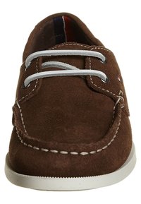 Zapato n�áutico marrón con cordones blancos, costuras blancas contrastantes y suela de goma blanca. Presenta un diseño sólido y punta redondeada.