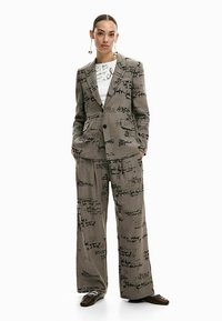 Gray suit with handwritten text patterns. The jacket features a single button and side pockets, and the pants are wide-legged in design.