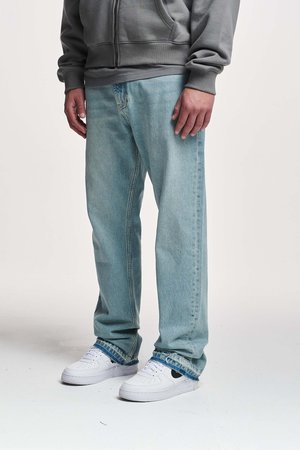 Vaqueros de denim azul claro con un corte relajado, que presentan una pierna recta y un dobladillo desgastado. Combinados con zapatillas blancas.