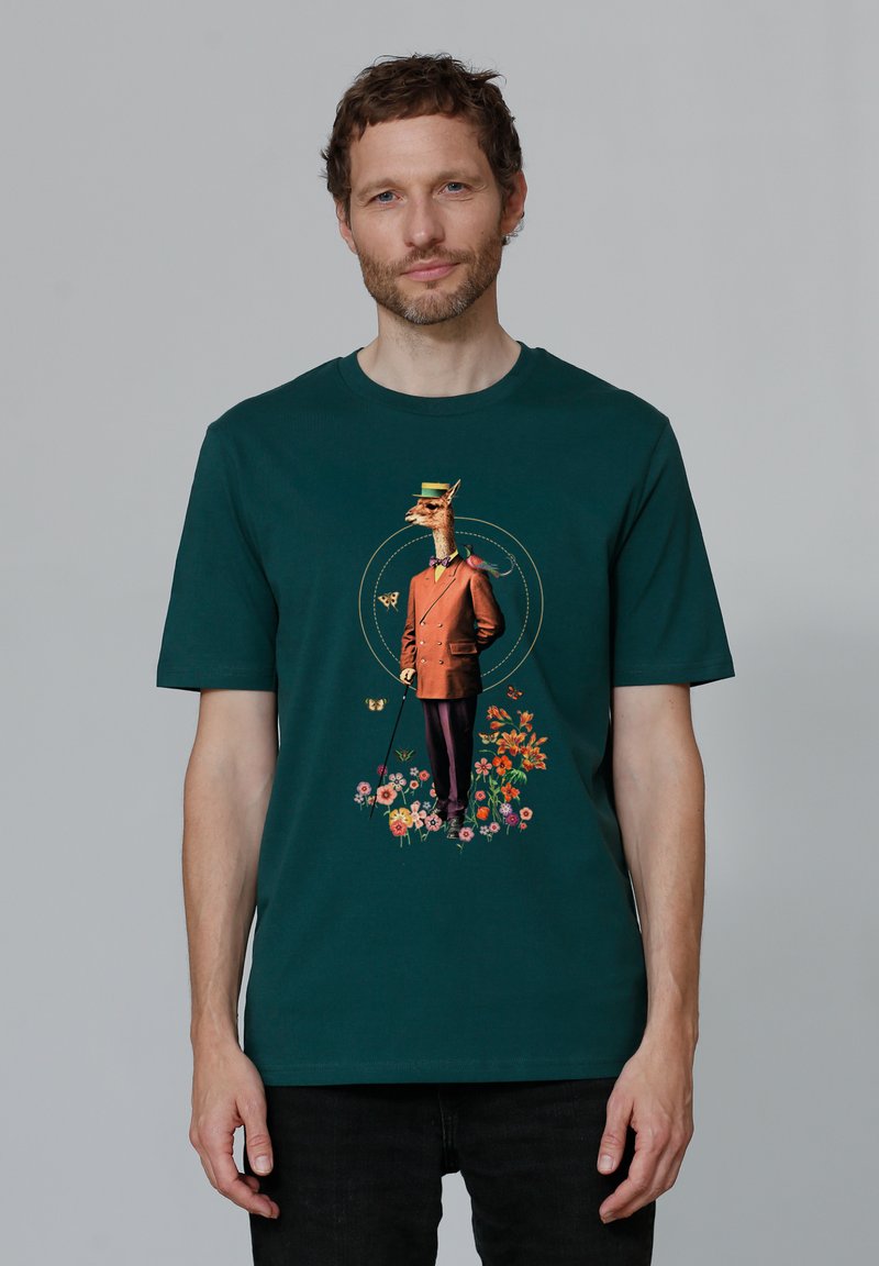 T-shirt en coton vert foncé avec un imprimé graphique d'une girafe en costume formel, des fleurs, des détails illustrés et des couleurs vives.