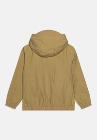 Giacca leggera color khaki con cappuccio, orlo elasticizzato arricciato e maniche lunghe. Realizzata in tessuto morbido con dettagli cuciti.