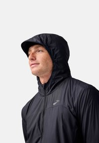 Giacca nera con cappuccio e chiusura a zip, caratterizzata da una texture liscia e leggera e un logo discreto sul petto.