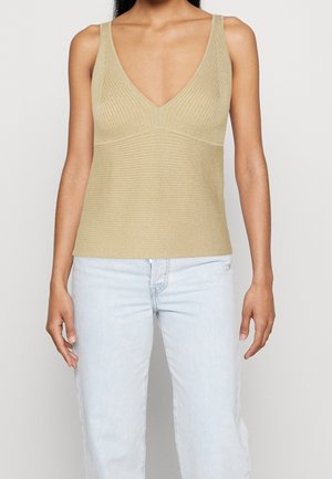 Kvinde iført en beige ribstrikket, ærmeløs top med dyb V-hals, kombineret med lyseblå højtaljede jeans.