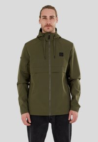 Veste imperméable vert olive avec fermeture éclair à l'avant, capuche ajustable et un patch logo noir, conçue avec une silhouette épurée.