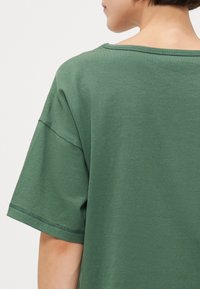 Groene katoenen t-shirt met een losse pasvorm, brede halslijn en korte mouwen met zichtbare stiksels langs de zoom en schoudernaden.
