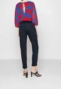 Blus med blommönster i rött och blått med en nyckelhålsknäppning bak, matchad med marinblå snäva byxor och svarta klacksandaler. Slät textur och åtsittande design.