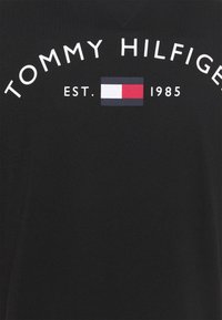 Camiseta de algodón negra con el texto blanco "TOMMY HILFIGER", la fecha de establecimiento "EST. 1985" y un logo tricolor en rojo, blanco y azul.