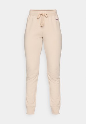 Pantalon de survêtement beige avec une taille élastique, cordon de serrage et poignets à côtes. Présente un petit logo sur le côté gauche près de la taille.