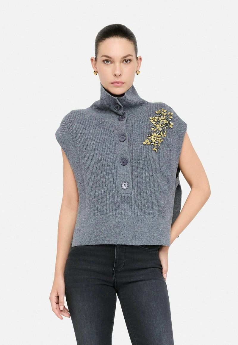 Top senza maniche grigio a maglia con colletto alto, dotato di chiusura a bottoni e decorazione con pietra gialla sul lato.