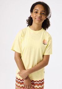 Geel T-shirt met korte mouwen en een ronde halslijn, met een subtiele textuur en een afgedrukte logo in oranje en zwart aan de linkerkant.