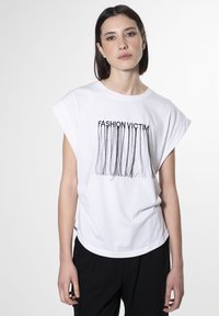 Hvid t-shirt i bomuld med korte ærmer, der har sort tekst "FASHION VICTIM" og lange frynser nederst. Casual fit.