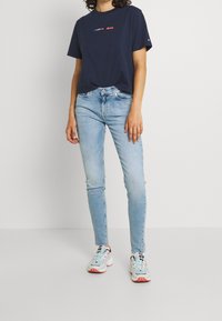 Camiseta de algodón azul marino con logotipo multicolor de "TOMMY JEANS", combinada con jeans ajustados de color azul claro y zapatillas deportivas multicolores.