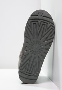 Sole di scarpa in gomma grigia con un motivo a zigzag testurizzato e un logo circolare al centro, caratterizzata da un design robusto e durevole.