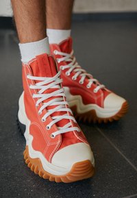 Sneakers alte in canvas arancione brillante con lacci bianchi. Presentano suole in gomma con un motivo ondulato e punte color crema.