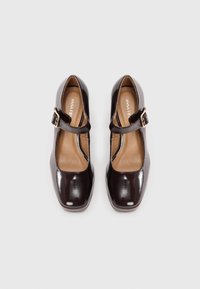 Mary Jane-style shoes in glossy dark brown patent leather. Square toe, adjustable strap with gold buckle, and tan insole.