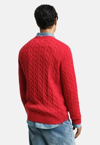 Rode kabelgebreide trui met geribbelde manchetten en onderkant, gedragen over een lichtblauw coll shirt, met een gestructureerd, geweven ontwerp.