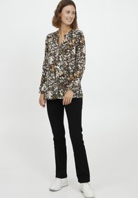 Blusa floreale con un motivo nero, bianco e arancione, con scollo a V e maniche lunghe. Abbinata a pantaloni neri e sneakers bianche.