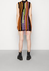Abito nero in maglia con strisce verticali colorate in arancione, verde, viola e rosa, con dettagli a taglio e frange all'orlo.