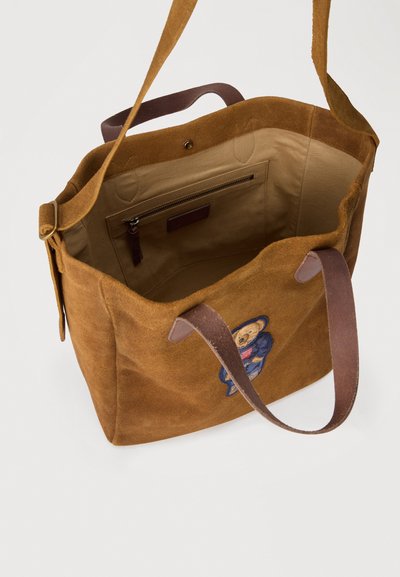 Borsa tote in camoscio marrone con manici in pelle, apertura superiore che mostra l'interno beige con tasca con zip e patch a forma di orsetto sulla parte anteriore.