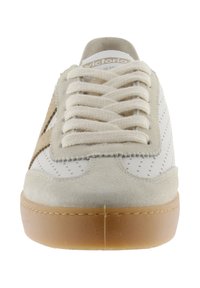 Zapatilla blanca y beige con cordones gruesos beige, laterales perforados, acentos de ante y suela de caucho marrón, vista desde el frente.