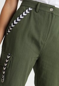 Gröna cargobyxor med ett zigzag-mönstrat svart och vitt sidostreck, metallbeslag och en avslappnad passform med flera fickor.