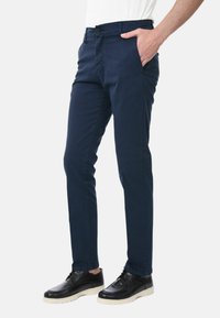 Pantaloni blu navy realizzati in tessuto di cotone liscio, con una vestibilità slim, tasche laterali e chiusura a un bottone. Abbinati a scarpe nere.